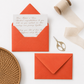 orange envelopes with a letter on a white surface, accompanied by scissors and ribbons.